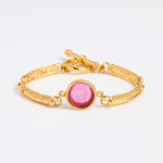 Gold link bracelet with round pendant in the centre with magenta glass