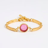 Gold link bracelet with round pendant in the centre with magenta glass