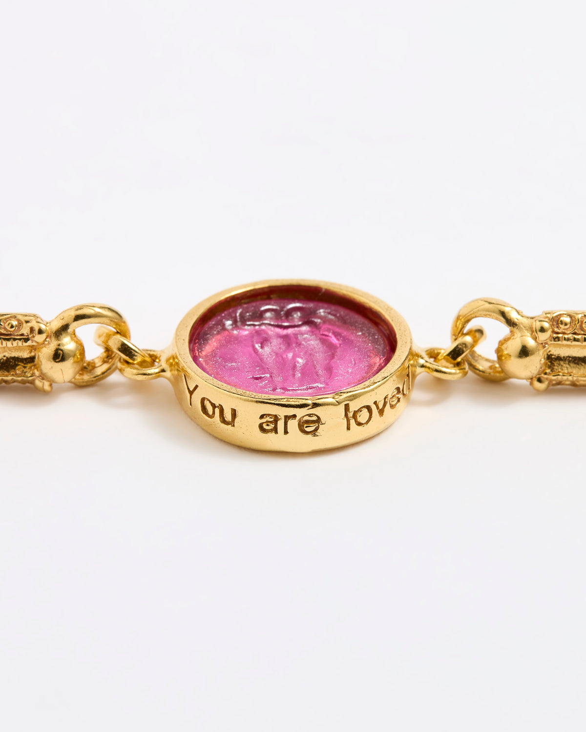 Gold link bracelet with round pendant in the centre with magenta glass and isciption 'you are loved' 