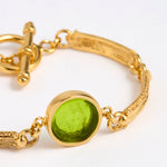 Close up Gold link bracelet with round pendant in the centre with green glass 