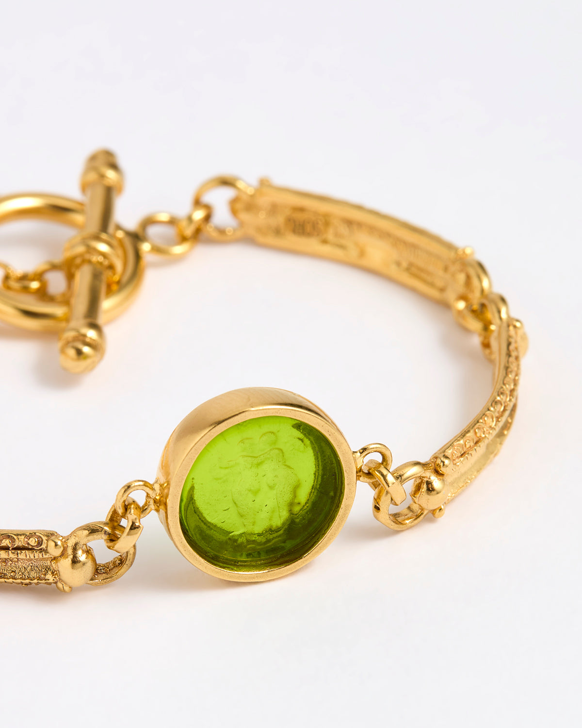 Close up Gold link bracelet with round pendant in the centre with green glass 
