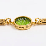 Gold link bracelet with round pendant in the centre with green glass and inscription on side ' you are loved'