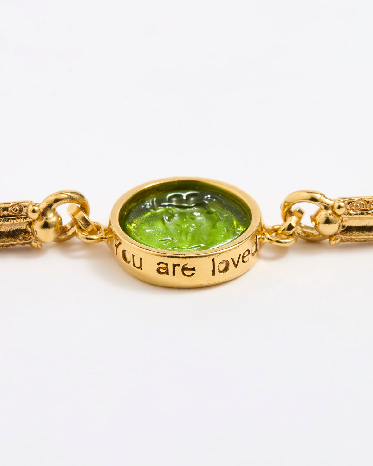 Gold link bracelet with round pendant in the centre with green glass and inscription on side ' you are loved'