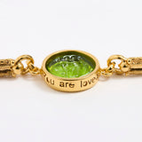 Gold link bracelet with round pendant in the centre with green glass and inscription on side ' you are loved'