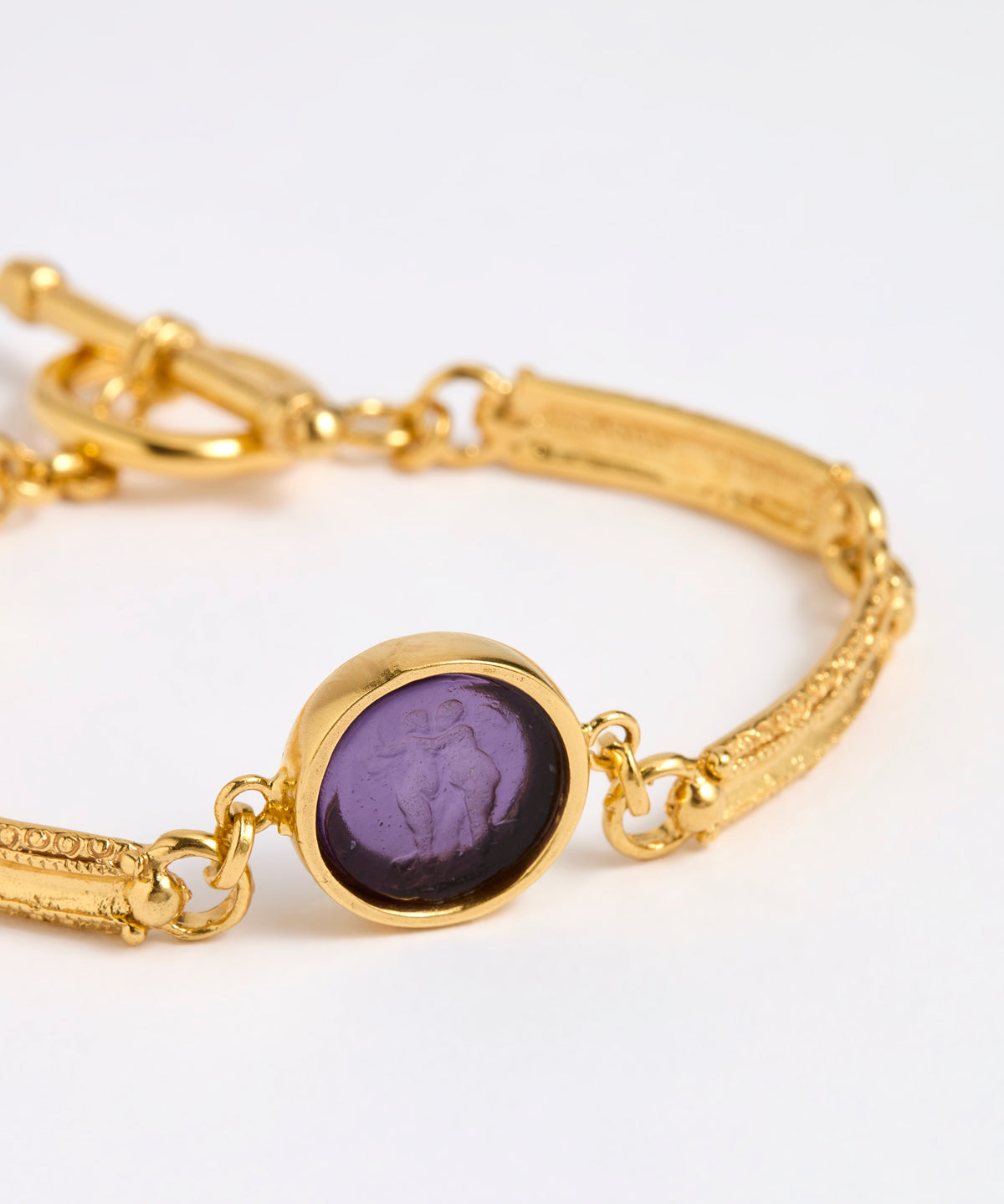 Close up of Gold link bracelet with round pendant in the centre with violet glass