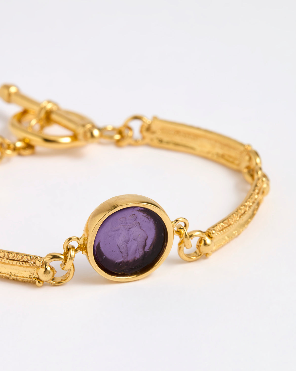 Close up of Gold link bracelet with round pendant in the centre with violet glass