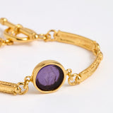 Close up of Gold link bracelet with round pendant in the centre with violet glass