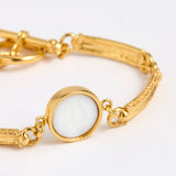 Close up of Gold link bracelet with round pendant in the centre with white glass