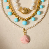 Three layered necklaces with pearls, blue beads, and shell pendants on a beige background