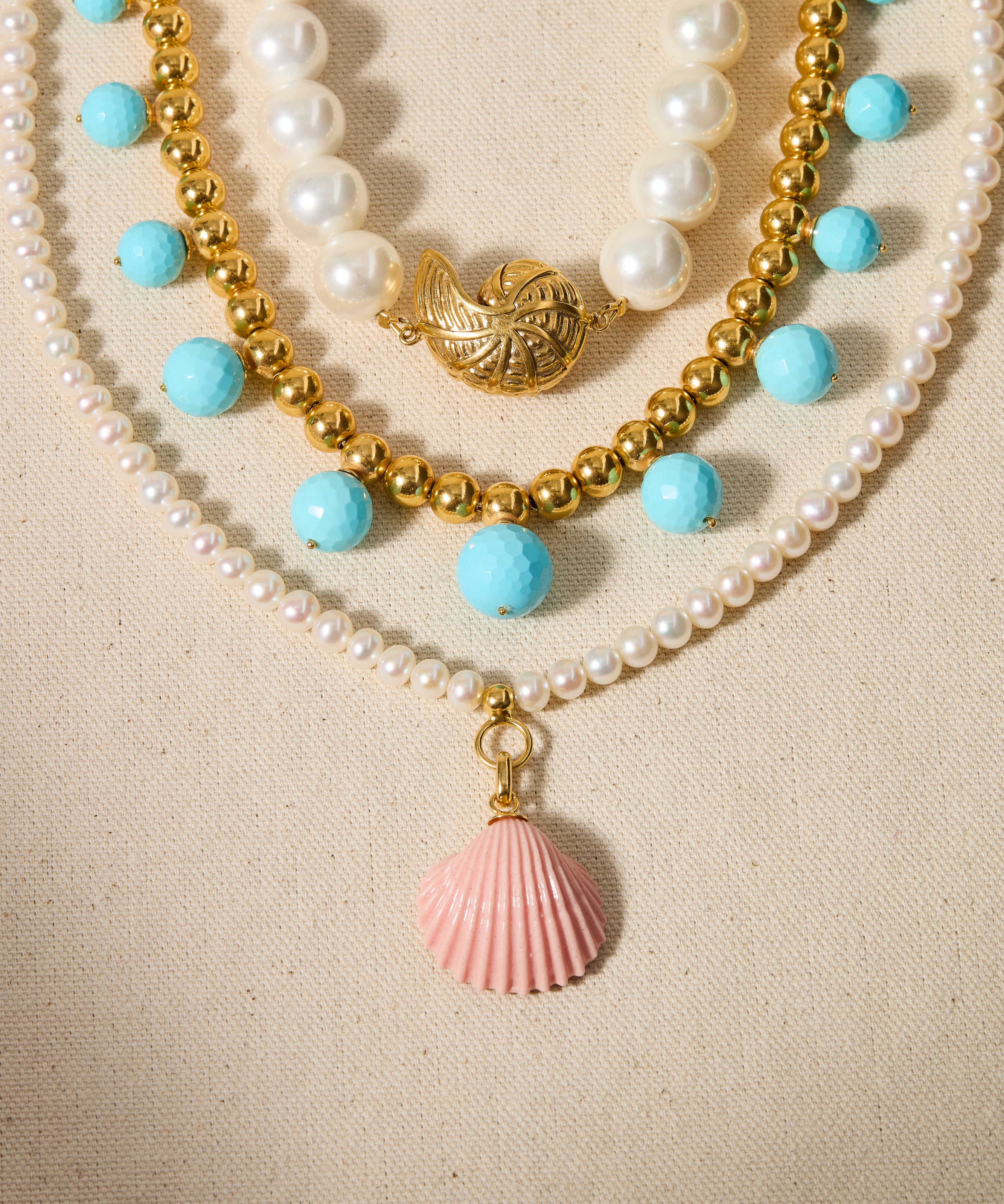Three layered necklaces with pearls, blue beads, and shell pendants on a beige background