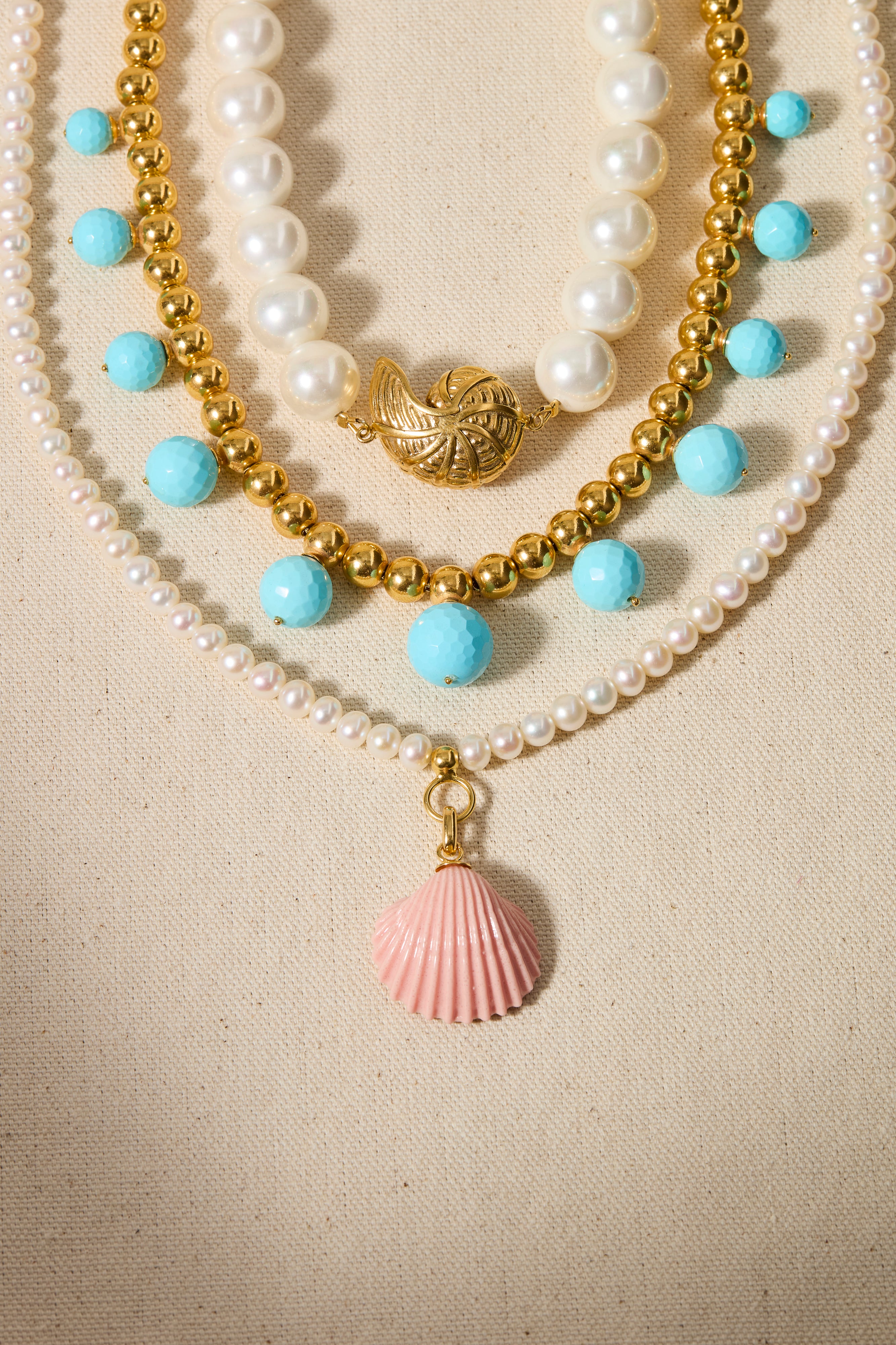 Three layered necklaces with pearls, blue beads, and shell pendants on a beige background