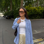 Woman in a blue striped shirt, white top, and beige pants standing on a street.