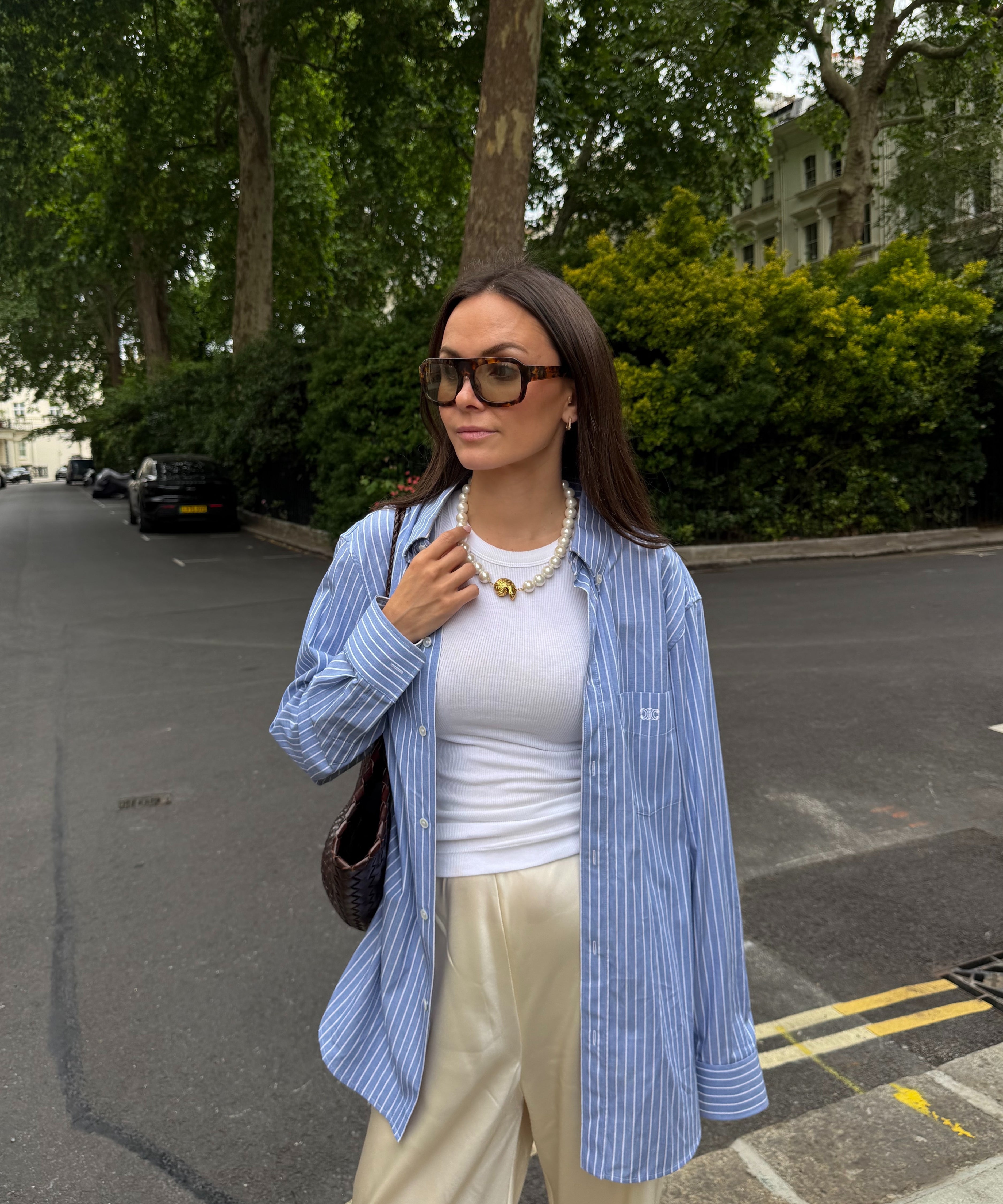 Woman in a blue striped shirt, white top, and beige pants standing on a street.
