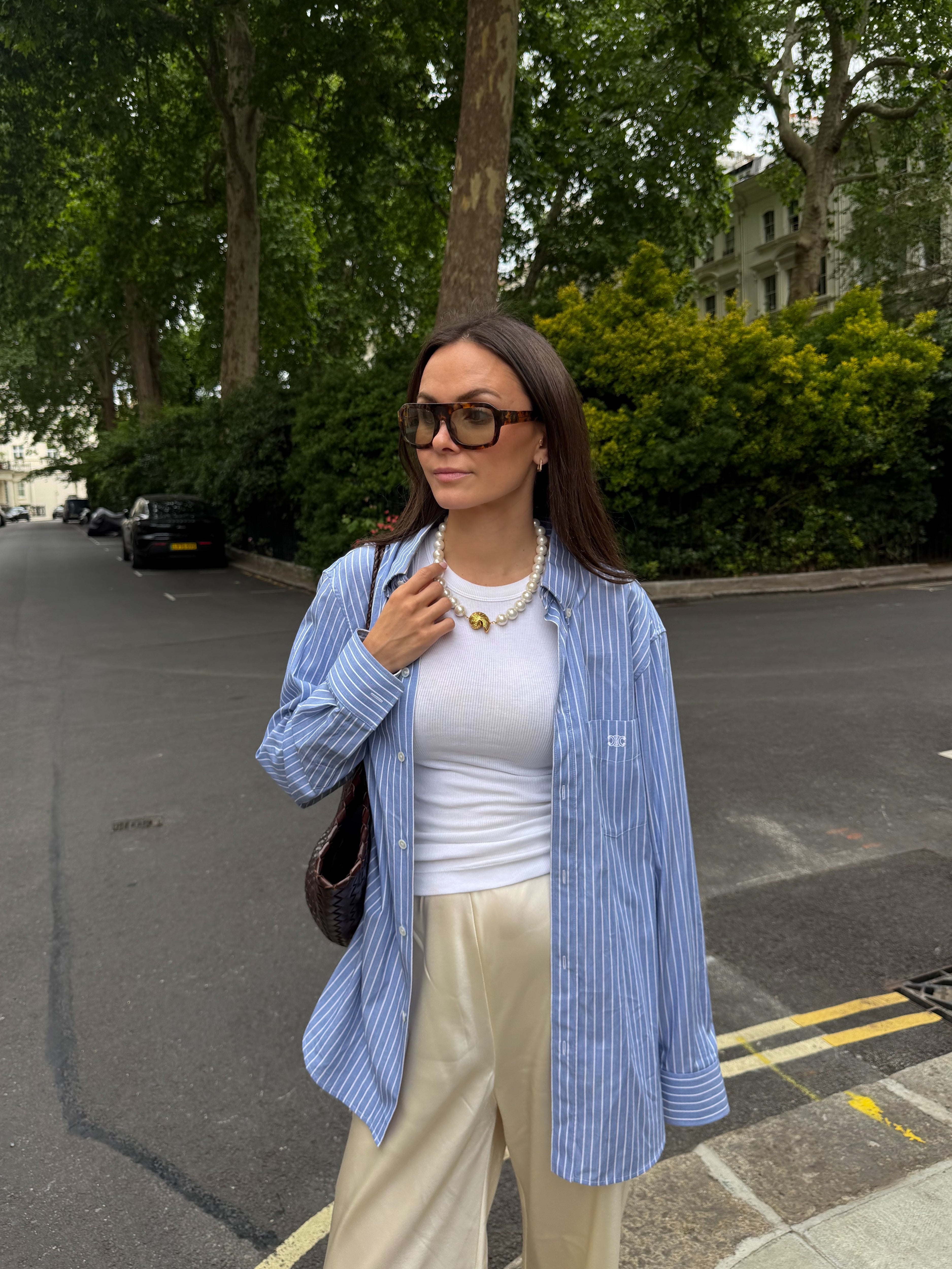 Woman in a blue striped shirt, white top, and beige pants standing on a street.