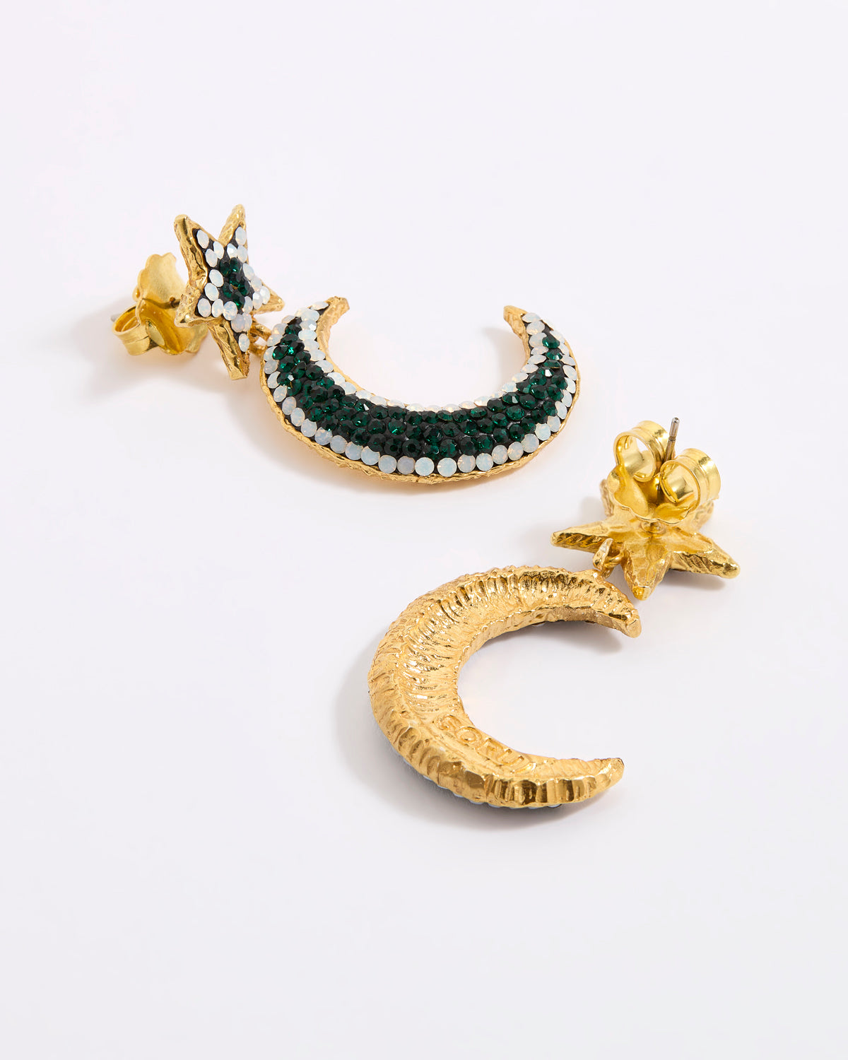 A pair of gold crescent moon and star earrings displayed against a white background. One earring is shown from the reverse, revealing a textured gold crescent moon, while the other features a gold crescent moon embellished with dark green and white opal rhinestones, complemented by a gold starburst post.