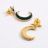 A pair of gold crescent moon and star earrings displayed against a white background. One earring is shown from the reverse, revealing a textured gold crescent moon, while the other features a gold crescent moon embellished with dark green and white opal rhinestones, complemented by a gold starburst post.