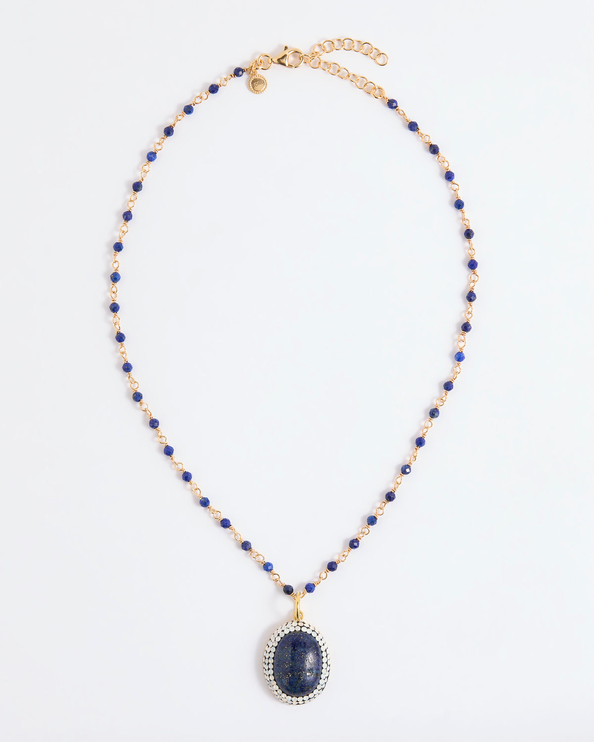 A beaded necklace featuring deep blue lapis lazuli stones and gold-toned spacer beads, with a large oval lapis lazuli pendant encircled by small white stones, displayed on a clean white background.