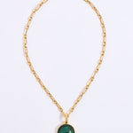 A gold chain necklace featuring a smooth, circular green malachite pendant, framed by a delicate border of sparkling green crystals, displayed against a white background.