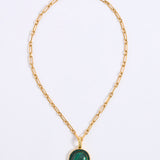 A gold chain necklace featuring a smooth, circular green malachite pendant, framed by a delicate border of sparkling green crystals, displayed against a white background.