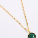 A gold chain necklace featuring a round pendant with a green malachite stone and a dark green crystal border, displayed on a white background.