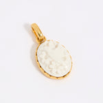 Gold coloured pendant with a white engraved design of a hummingbird on a light grey background