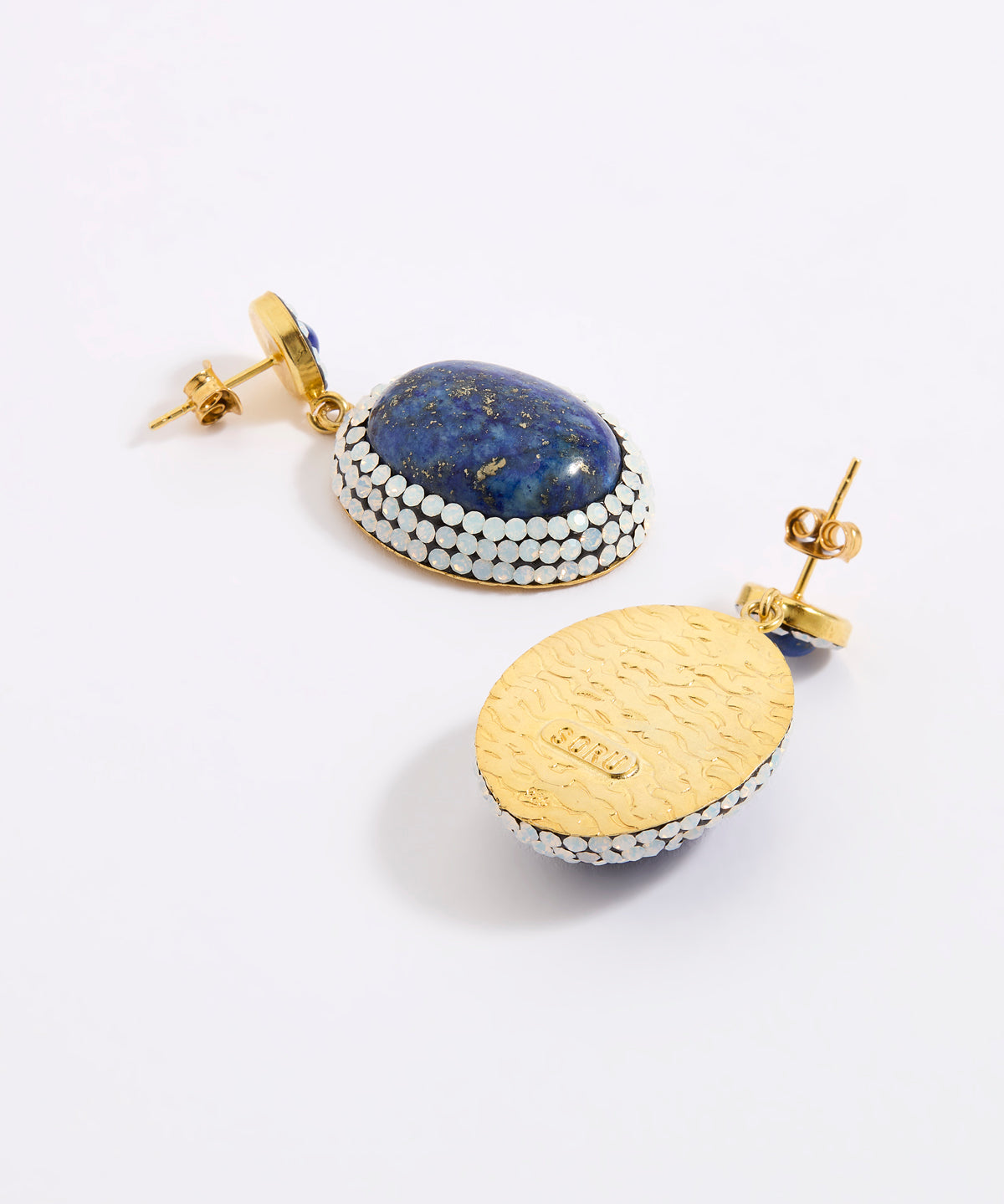 A pair of gold and lapis lazuli earrings shown on a white background, with one earring facing forward to display the blue lapis lazuli stone and white opal crystal border, and the other showing the textured gold back with a post.