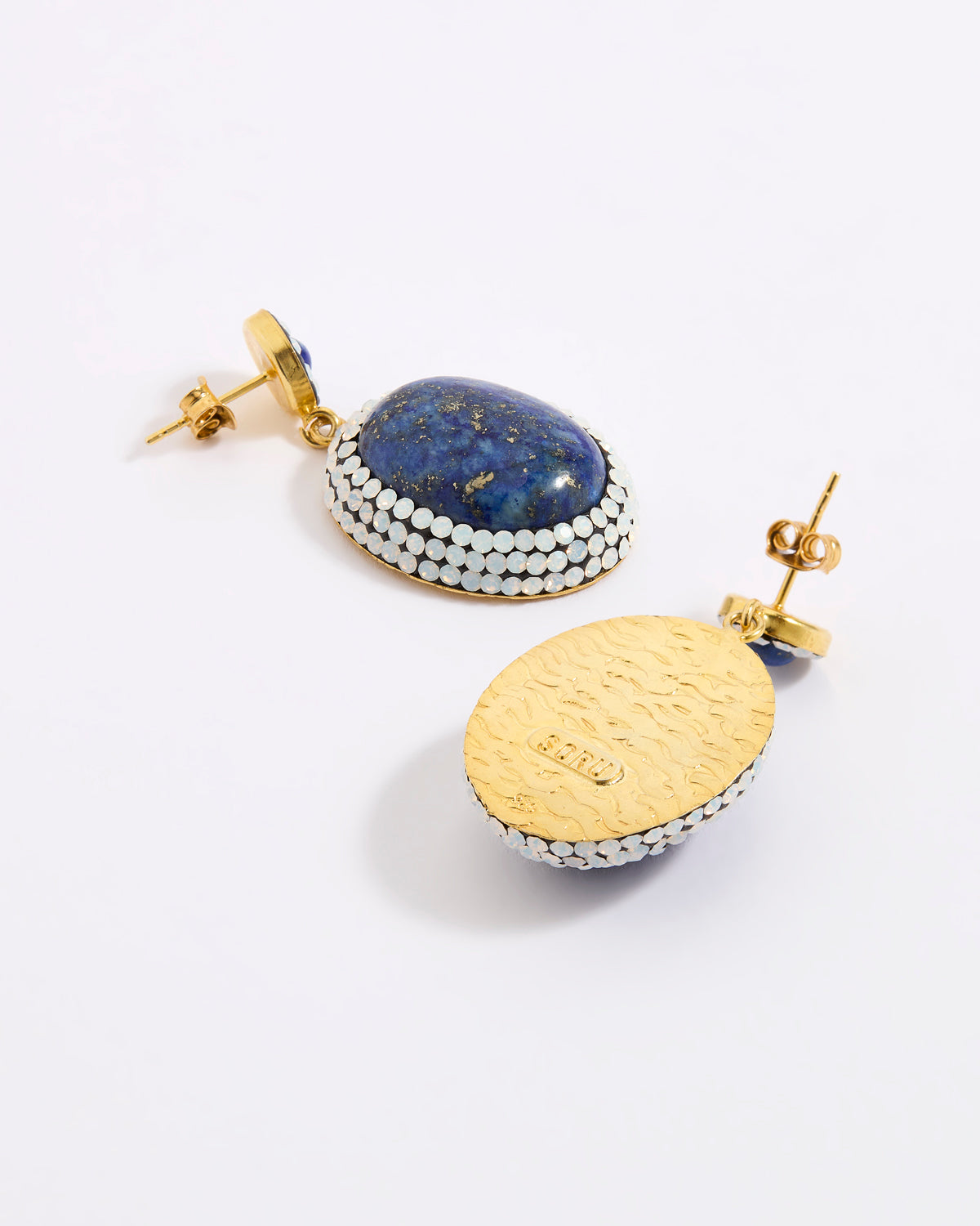 A pair of gold and lapis lazuli earrings shown on a white background, with one earring facing forward to display the blue lapis lazuli stone and white opal crystal border, and the other showing the textured gold back with a post.