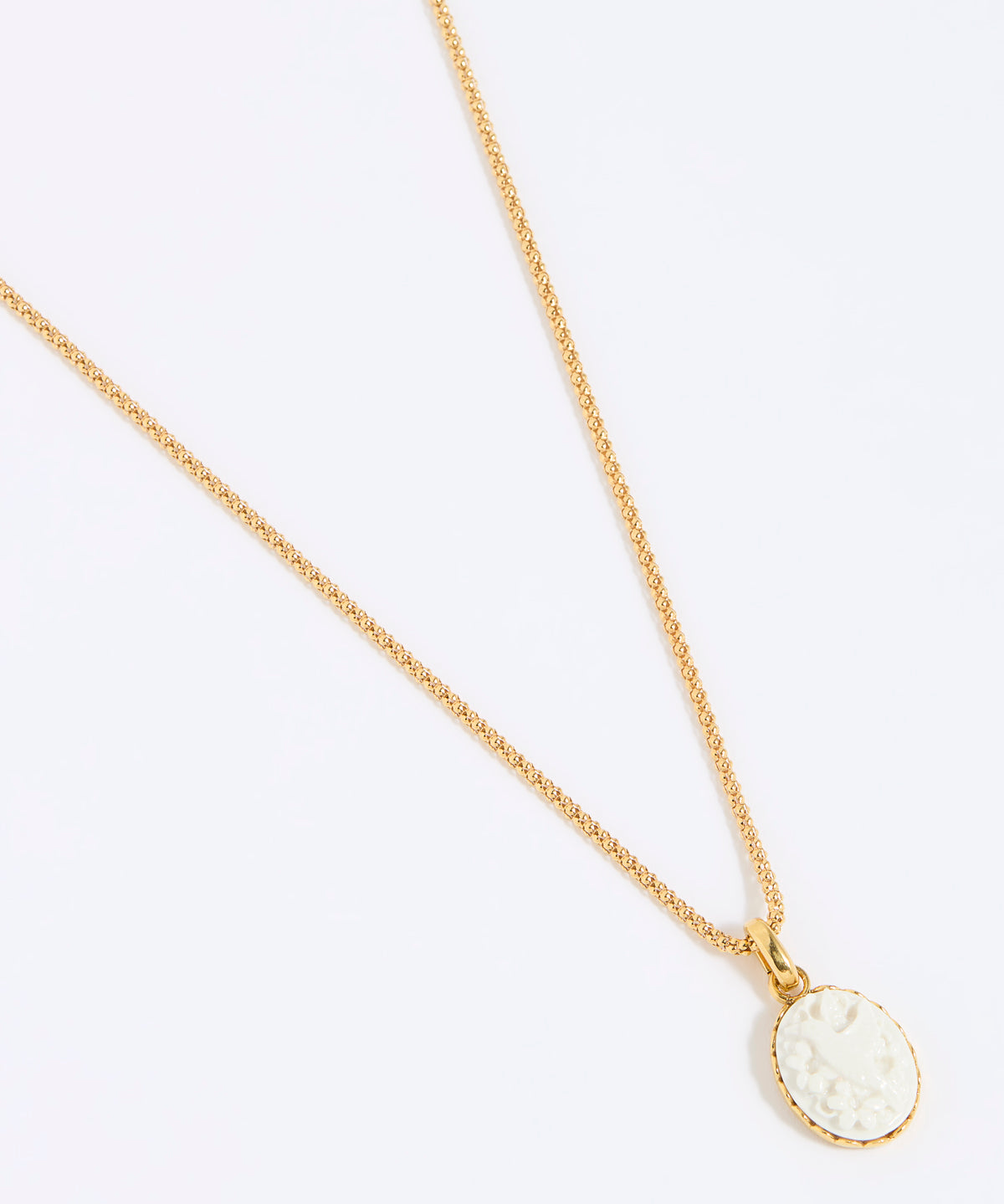 Gold coloured necklace with a round, white pendant of a hummingbird on a light grey background