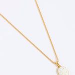 Gold coloured necklace with a round, white pendant of a hummingbird on a light grey background