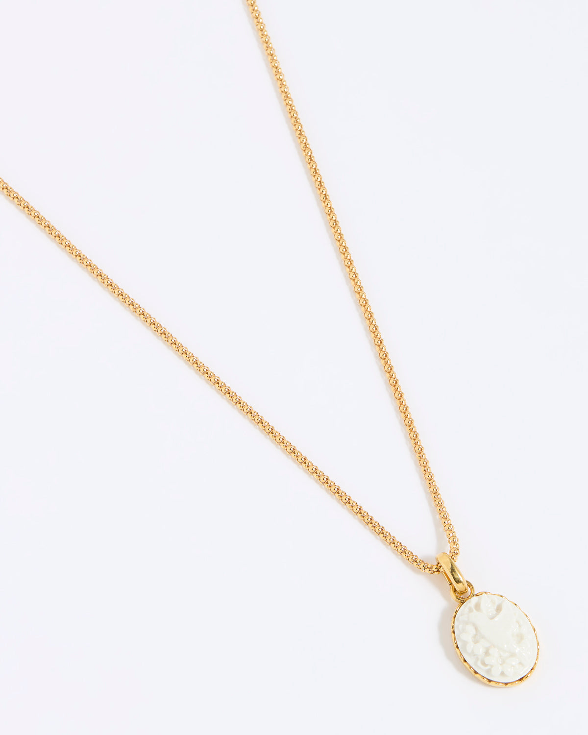 Gold coloured necklace with a round, white pendant of a hummingbird on a light grey background