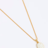 Gold coloured necklace with a round, white pendant of a hummingbird on a light grey background