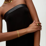 Woman wearing a black strapless dress with gold jewelry on a white background