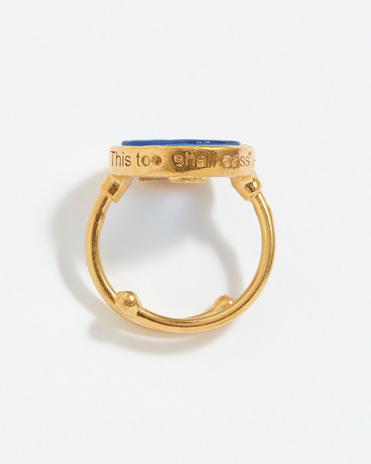 Gold ring with blue stone with "This Too Shall Pass" engraved on a white background