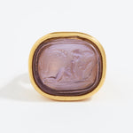 Gold ring with a purple stone featuring an engraved design on a white background