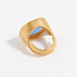 Gold textured ring with a blue stone on a light gray background