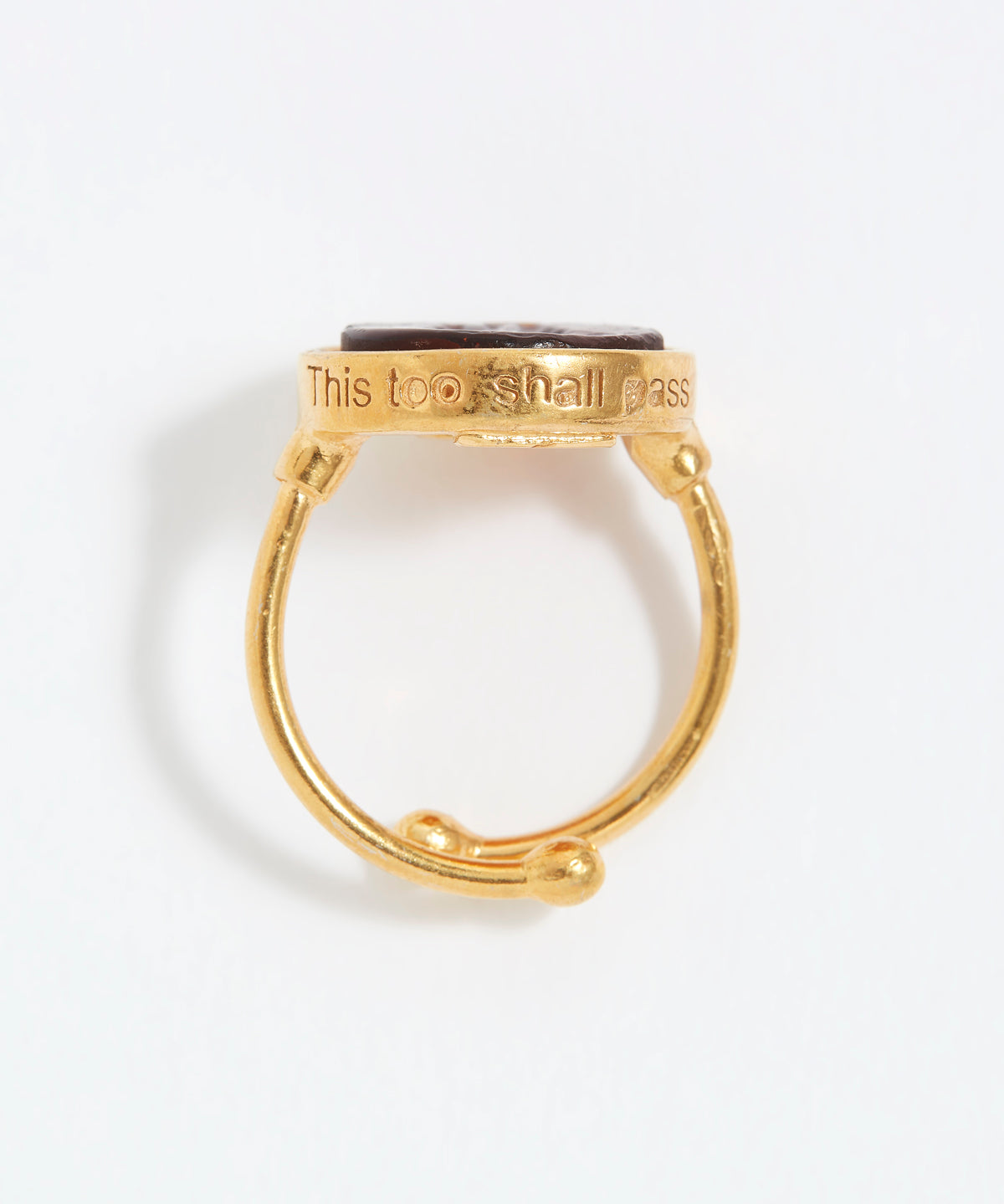 Gold ring with engraved text "This Too Shall Pass" on a white background