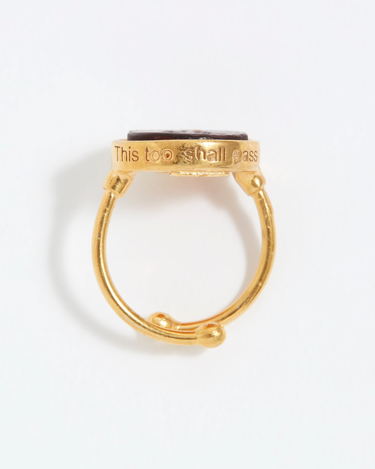 Gold ring with engraved text "This Too Shall Pass" on a white background