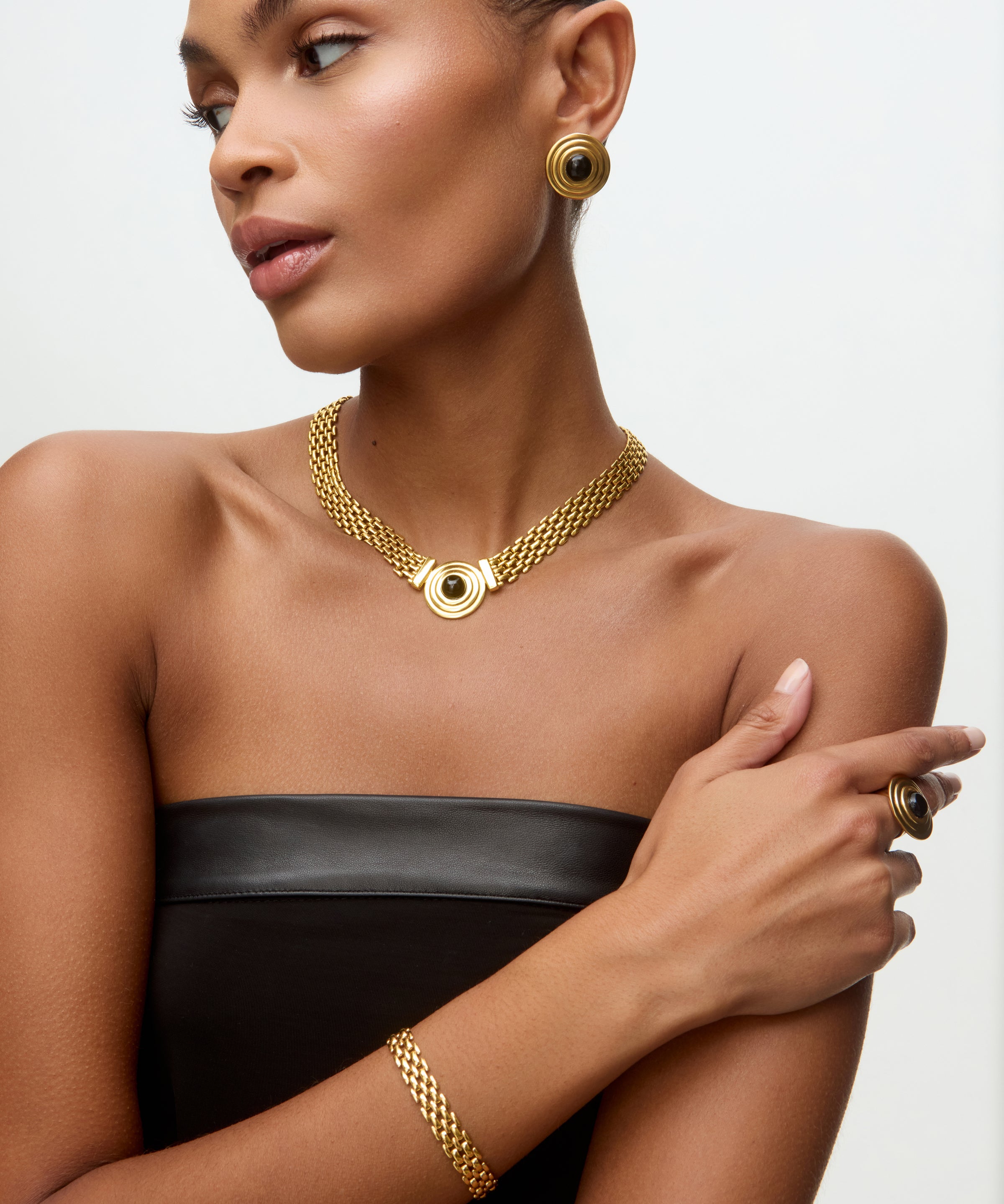 Image of a lady wearing black dress, gold chain bracelet, matching choker with round onyx detail and matching stud earrings.
