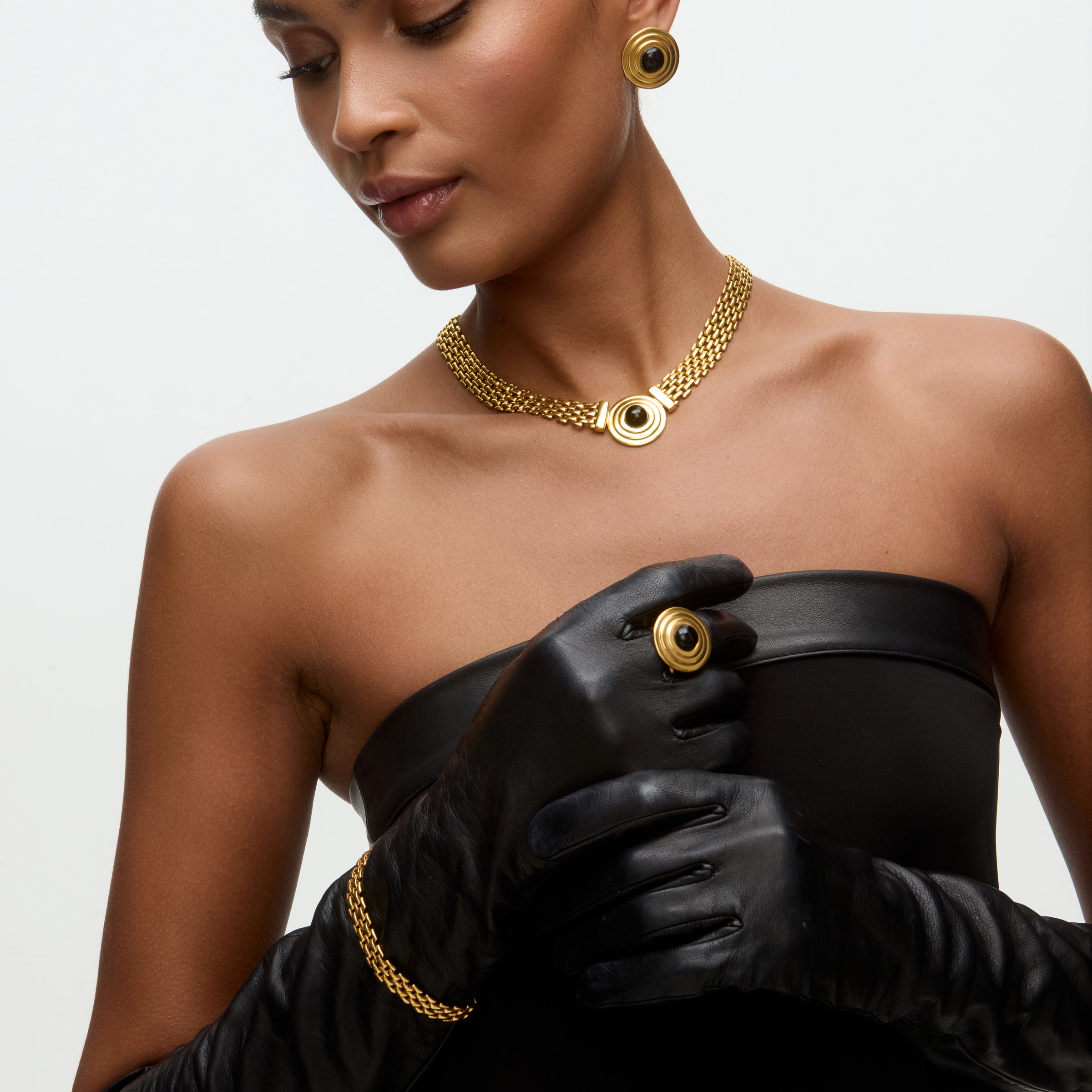 Image of a lady wearing black dress, gold chain bracelet, matching choker with round onyx detail and matching stud earrings.