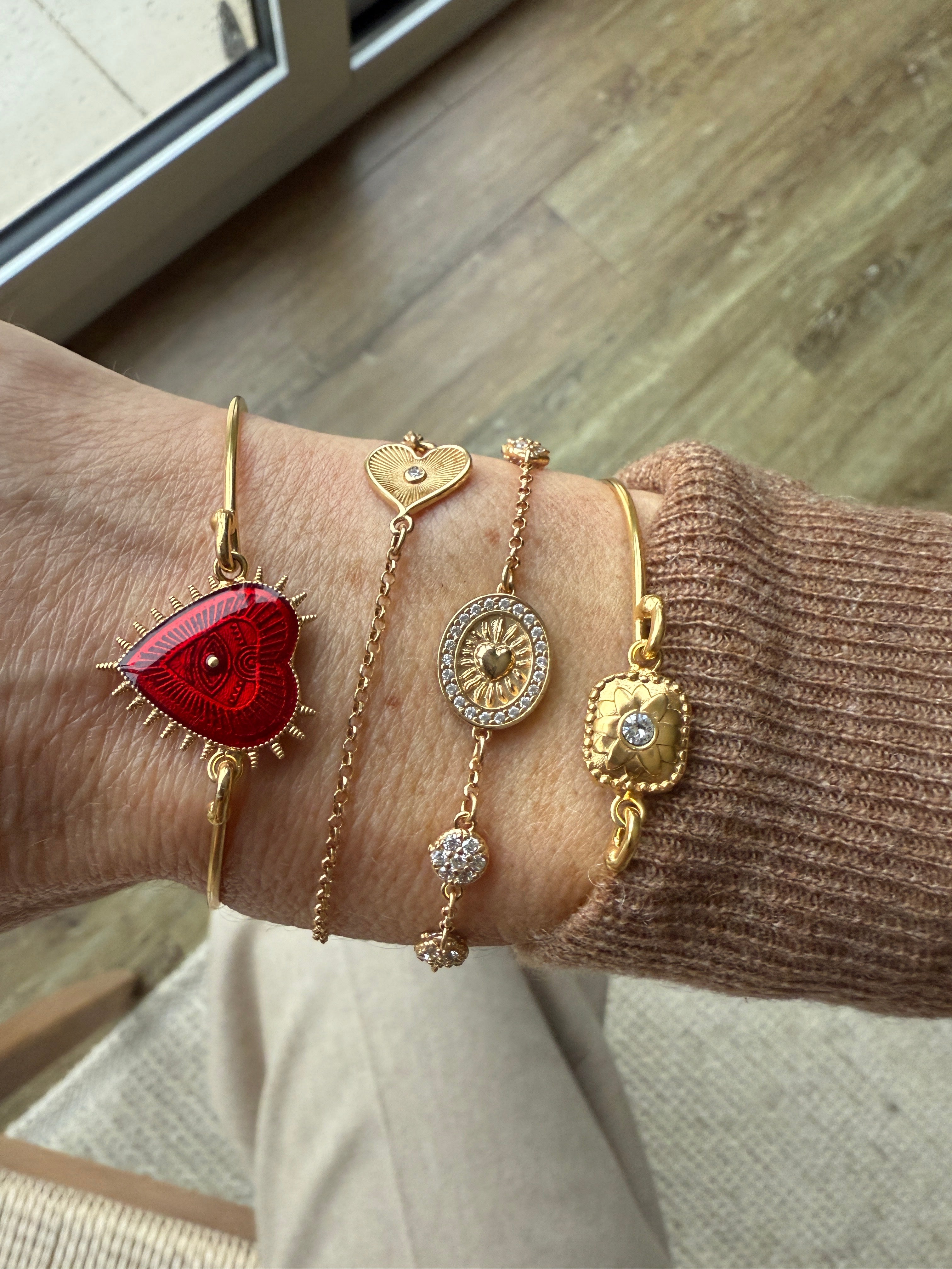 Image of wrist, wearing Romanza heart bracelet and a selection of delicate gold bracelets.