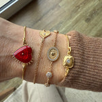 Image of wrist, wearing Romanza heart bracelet and a selection of delicate gold bracelets.