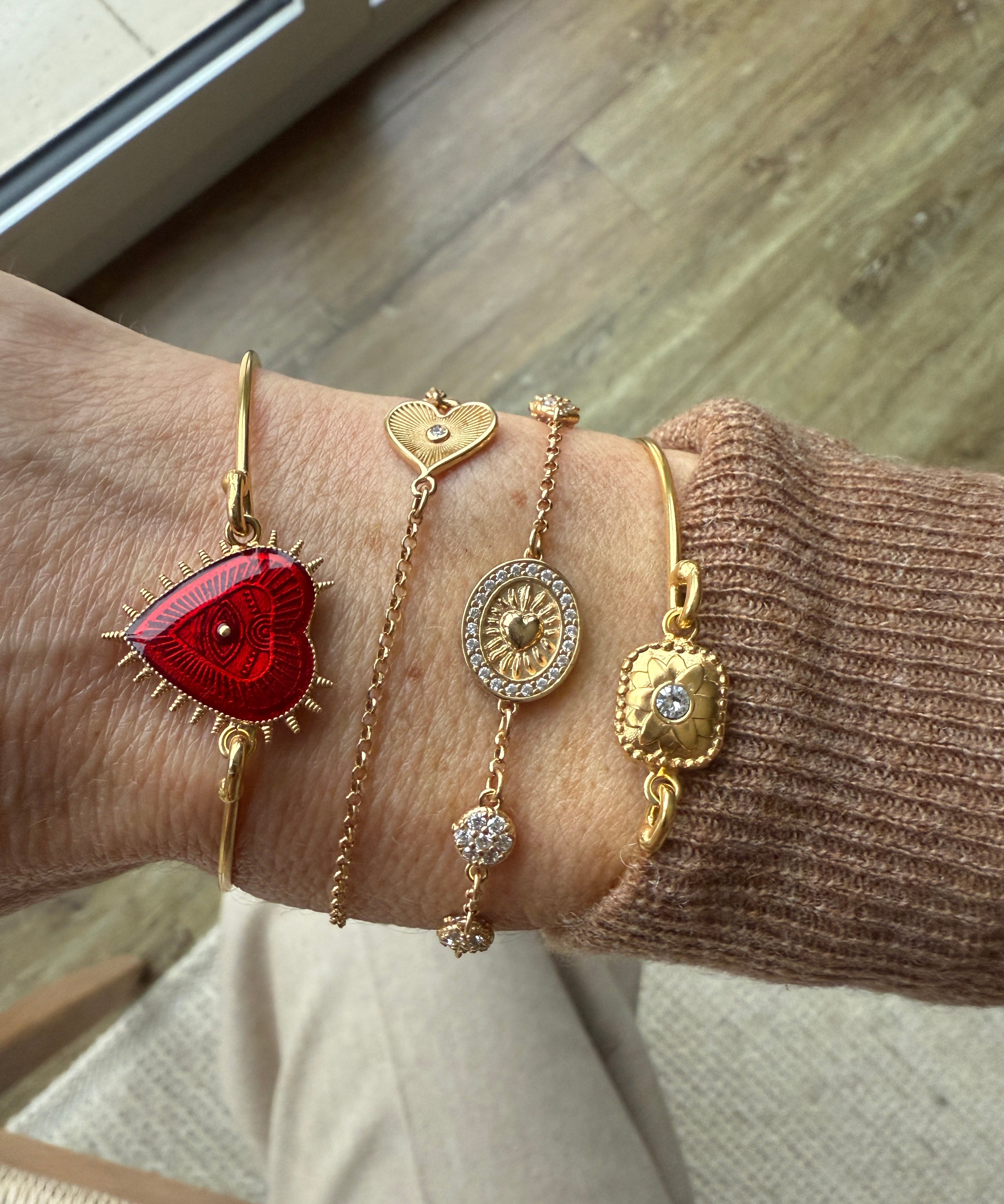 Image of wrist, wearing Romanza heart bracelet and a selection of delicate gold bracelets.