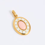 Oval gold coloured pendant with a pink center on a light grey background