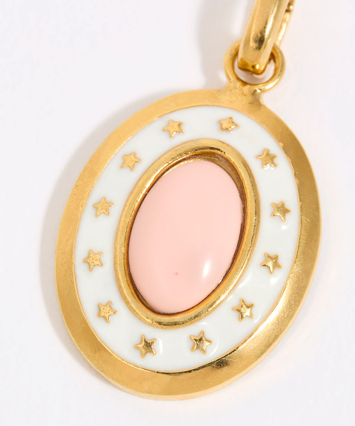 Gold coloured pendant with a pink central stone and star accents on a white background
