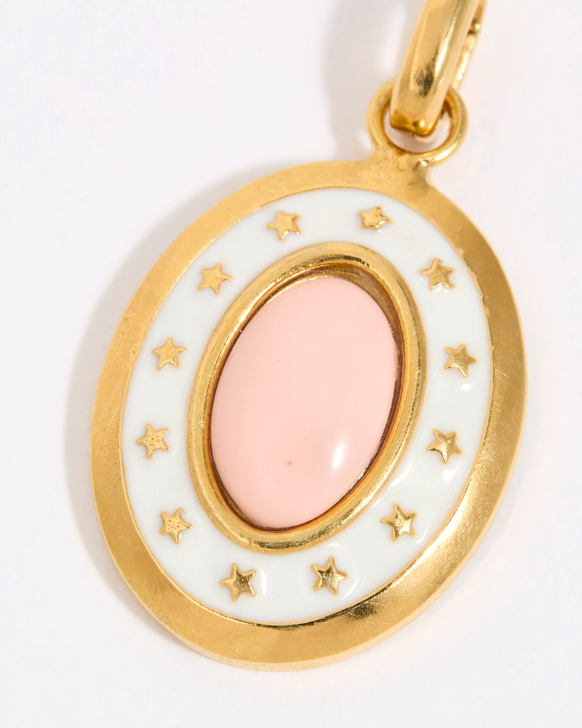 Gold coloured pendant with a pink central stone and star accents on a white background