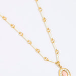 Gold coloured and white enamel necklace with a pink pendant on a white background
