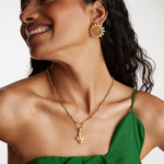 model wearing crystal embellished coin stud earrings with a charm chain necklace and a chunky cross charm.