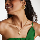 model wearing crystal embellished coin stud earrings with a charm chain necklace and a chunky cross charm.