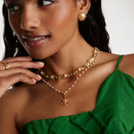 model image wearing soru jewellery ships wheel charm on a pearl charm chain, layered with pearl and crystal necklace and gold stud earrings