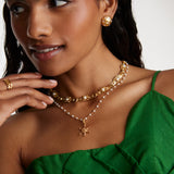 model image wearing soru jewellery ships wheel charm on a pearl charm chain, layered with pearl and crystal necklace and gold stud earrings